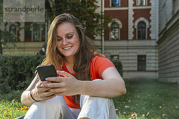 Glückliche junge Frau  die vor dem Gebäude ihr Mobiltelefon benutzt