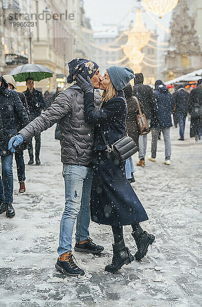 Paar küsst sich im Schnee auf dem Weihnachtsmarkt