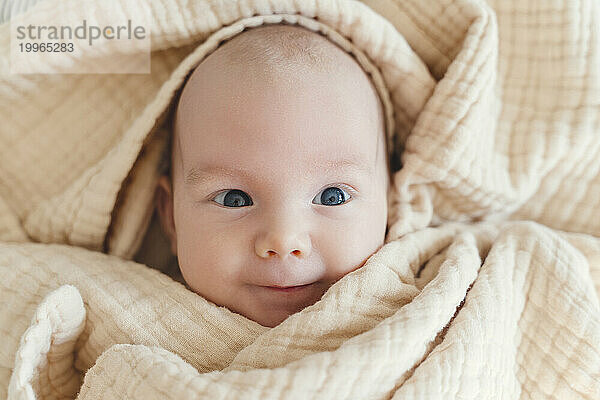 Lächelnder süßer Junge  in eine Decke gehüllt