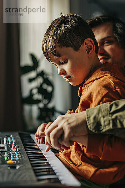 Vater hält Händchen und bringt seinem Sohn zu Hause E-Piano bei