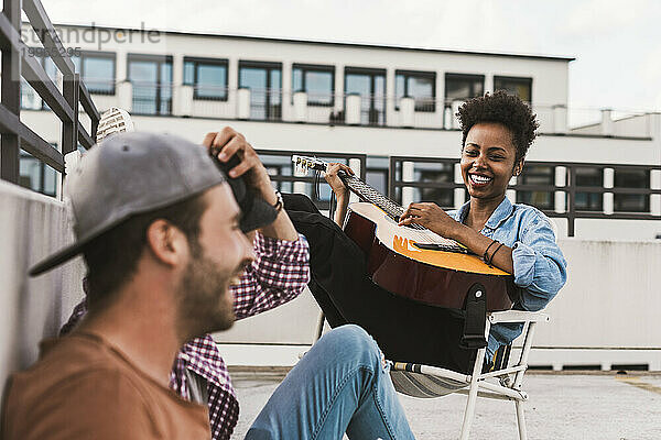 Lächelnde Frau spielt Gitarre in der Nähe von Freunden auf der Terrasse