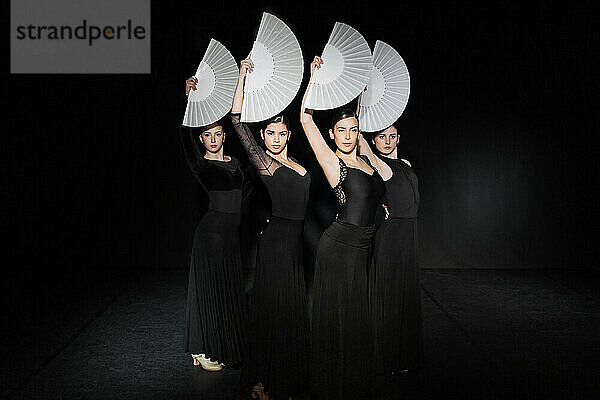 Schöne Flamencoschüler tanzen gemeinsam vor schwarzem Hintergrund