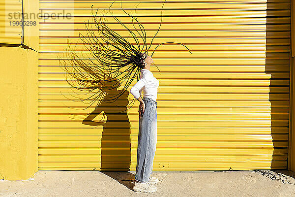 Woman tossing hair in front of yellow corrugated shutter