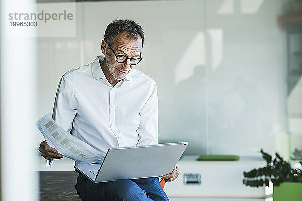 Geschäftsmann sitzt mit Grafik und benutzt Laptop im Büro