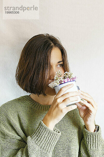 Schöne Frau riecht Blumen aus einer Tasse vor weißem Hintergrund