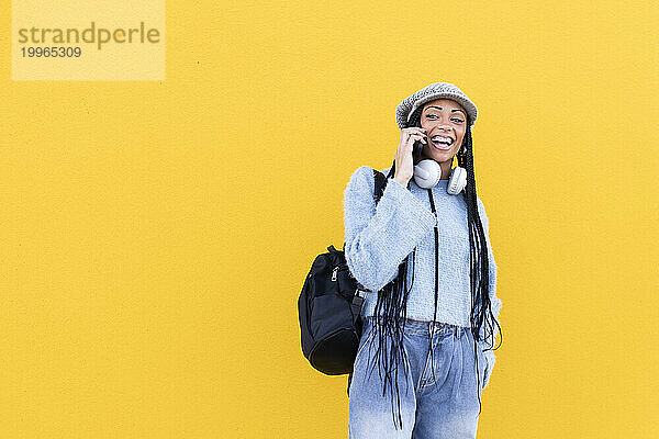 Fröhliche Frau  die vor einer gelben Wand mit ihrem Smartphone spricht