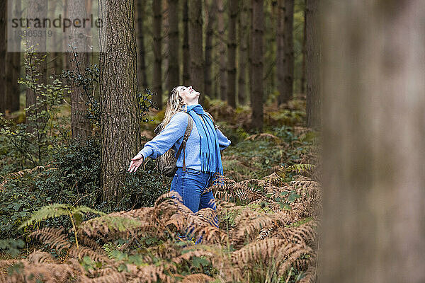 Glückliche junge Frau steht mit ausgestreckten Armen im Cannock Chase Forest