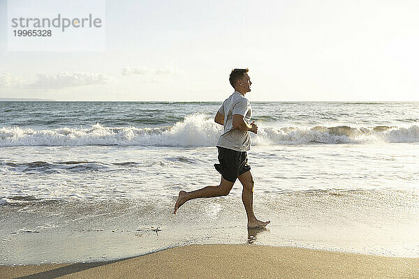 Junger Mann läuft bei Sonnenuntergang am Meer