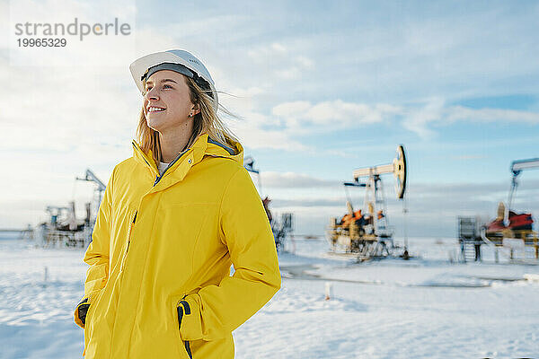 Lächelnder Ingenieur steht im Winter am Ölförderfeld