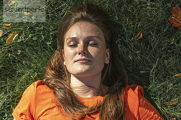 Smiling redhead woman with sunlight over face relaxing on grass