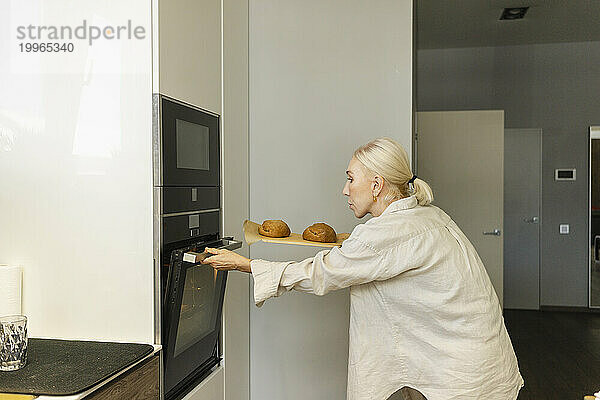 Reife Frau öffnet Ofen  um zu Hause Brot zu backen