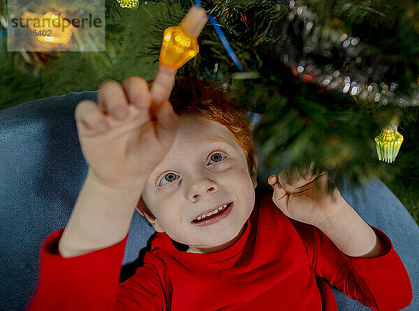Netter Junge spielt mit Weihnachtsbeleuchtung unter dem Baum