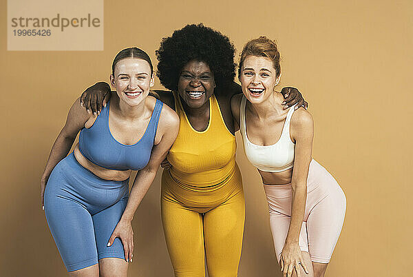 Cheerful woman with arms around female friends against beige background