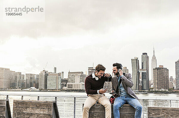 Zufriedene Geschäftskollegen tragen Kopfhörer und hören Musik vor der Skyline von New York City