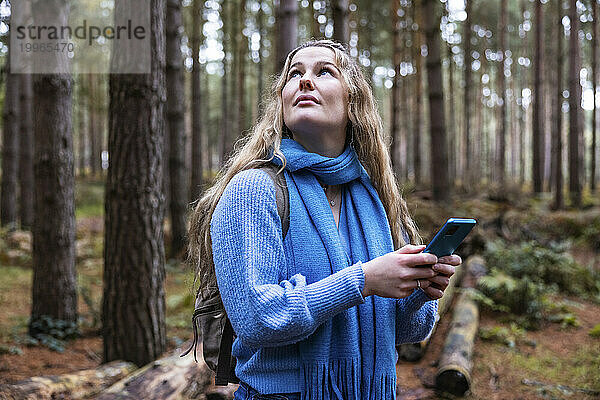 Nachdenkliche Frau mit Smartphone im Cannock Chase Forest