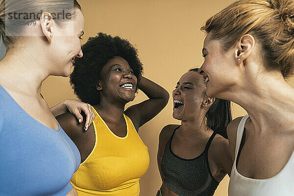 Fröhliche  gemischtrassige Freundinnen  die vor beigem Hintergrund lachen