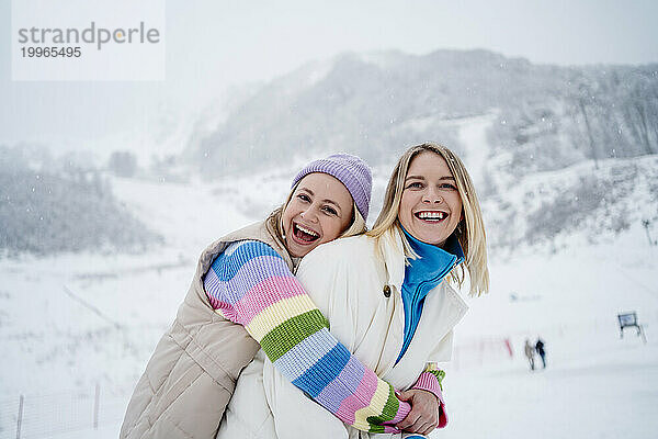 Lächelnde Frau umarmt Freundin auf schneebedecktem Berg