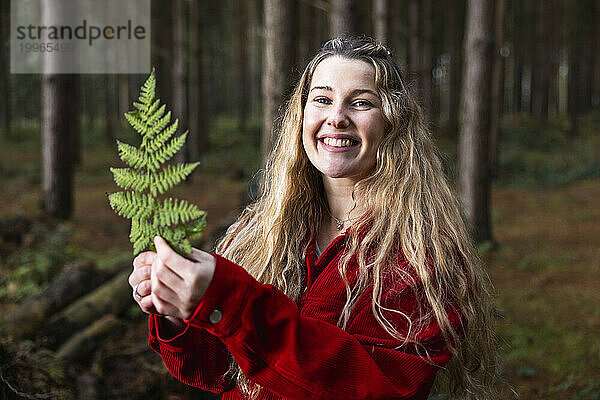 Glückliche schöne Frau hält Farnblatt im Wald von Cannock Chase