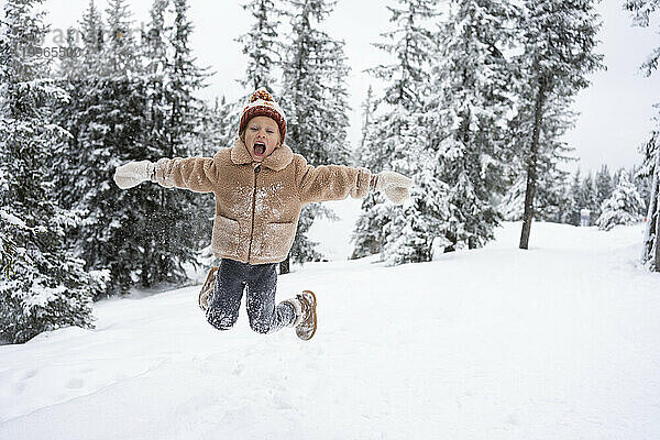 Glückliches Mädchen  das im Winterwald auf Schnee springt