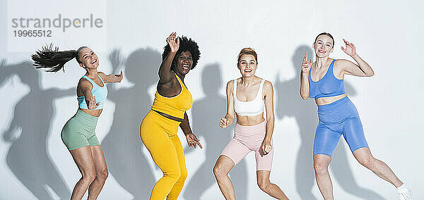 Excited multiracial female friends dancing together against white background