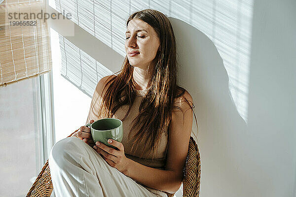 Frau mit Kaffeetasse entspannt sich im Stuhl am Fenster