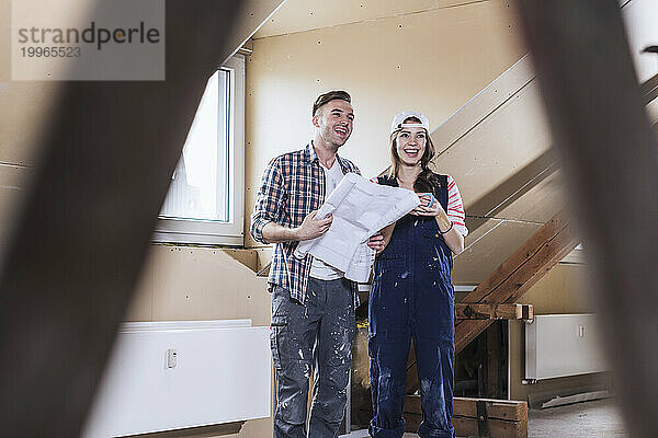 Smiling couple holding blueprint at home