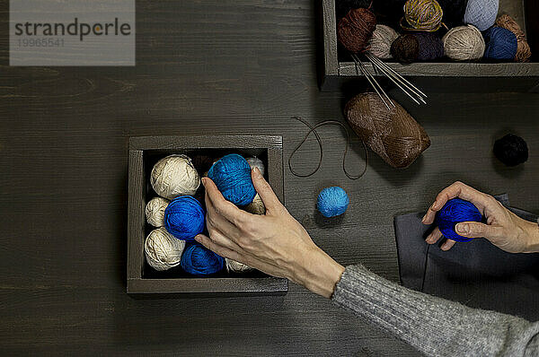 Woman picking up yarn balls from table
