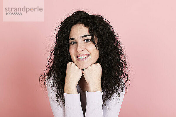 Smiling young woman with hands on chin against pink background
