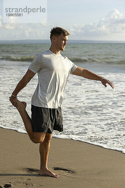 Junger Mann streckt Bein am Strand