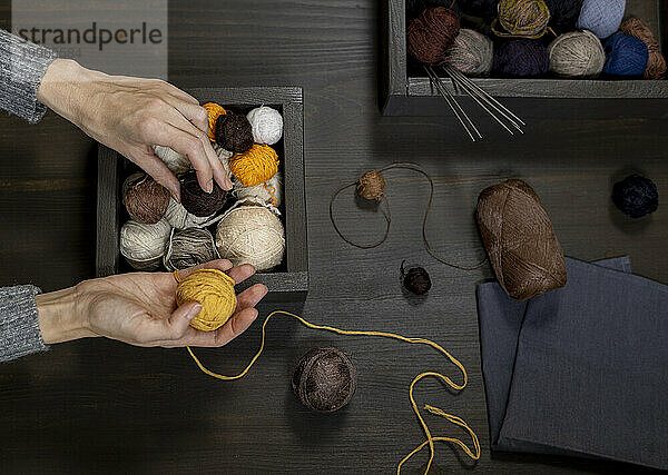 Hands of woman choosing balls of yarn on table