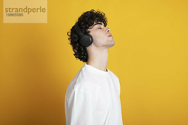 Junger Mann hört Musik mit geschlossenen Augen vor gelbem Hintergrund