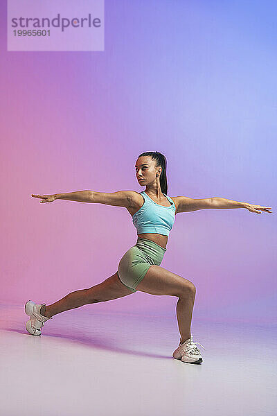 Selbstbewusste junge Frau übt Krieger-2-Position vor farbigem Hintergrund