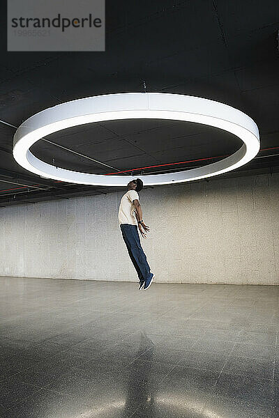 Junger Mann mit futuristischer Cyberbrille springt unter moderne Ringlampe