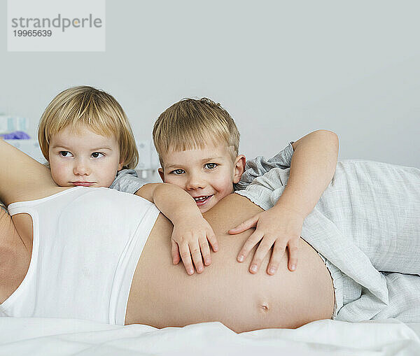 Kinder umarmen den Bauch der schwangeren Mutter zu Hause im Bett