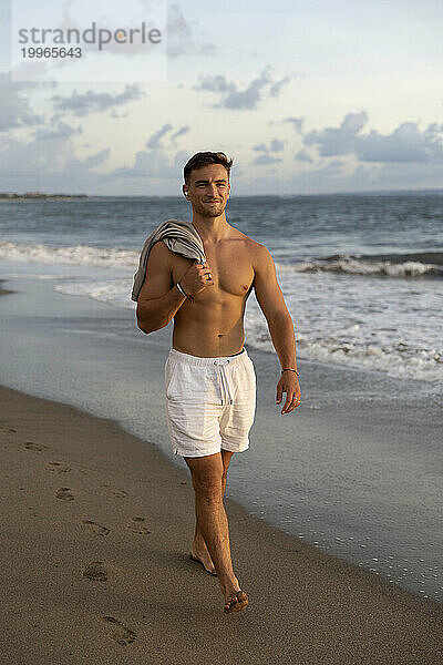 Lächelnder Mann ohne Hemd  der am Strand spaziert