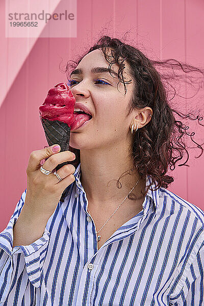 Glückliche Frau leckt Eis vor rosa Wand