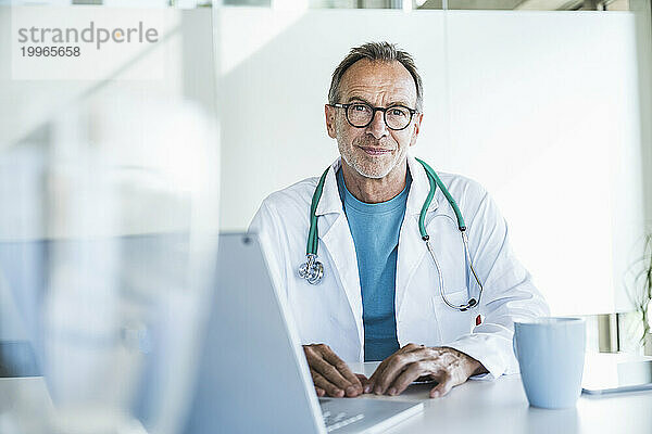 Lächelnder Oberarzt sitzt am Schreibtisch