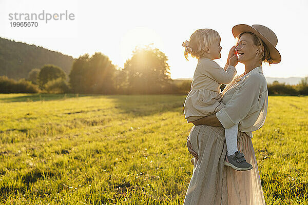 Lächelnde schwangere Frau mit Tochter im Feld