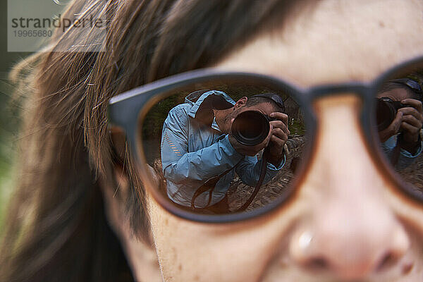 Spiegelbild eines Mannes  der mit der Kamera auf der Sonnenbrille einer Frau fotografiert