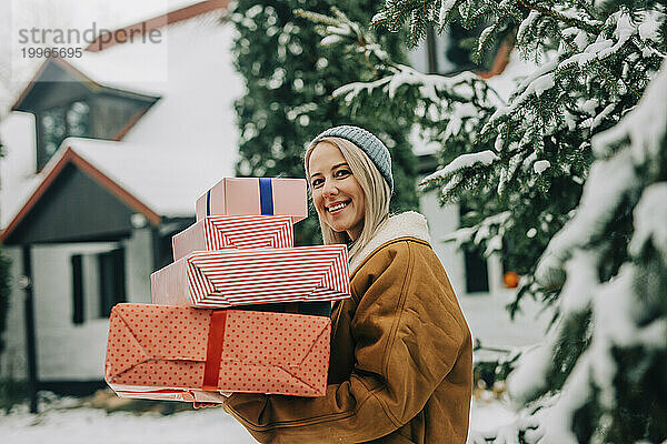 Glückliche Frau trägt Weihnachtsgeschenke neben Baum