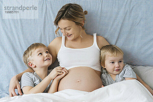 Lächelnde schwangere Mutter umarmt Kinder zu Hause im Bett