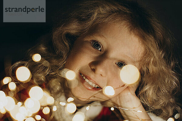 Smiling blond girl looking through string lights