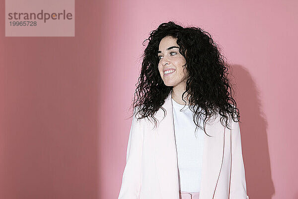 Smiling woman wearing blazer standing against pink background