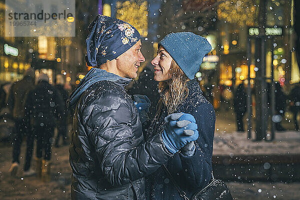 Lächelndes Paar tanzt im Schnee auf dem Weihnachtsmarkt