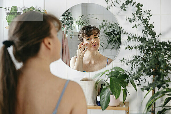 Woman applying cream on face in front of mirror