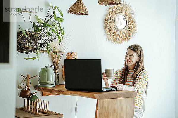 Lächelnde Frau mit Kaffeetasse und Laptop zu Hause