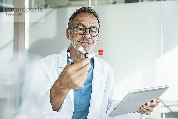 Lächelnder Mann im Laborkittel hält Tablet-PC in der Hand und untersucht die molekulare Struktur