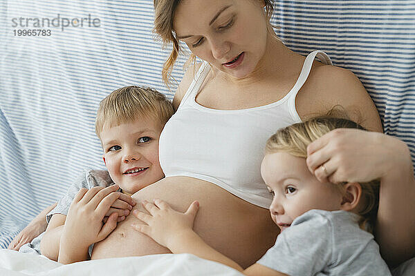 Pregnant mother embracing children at home