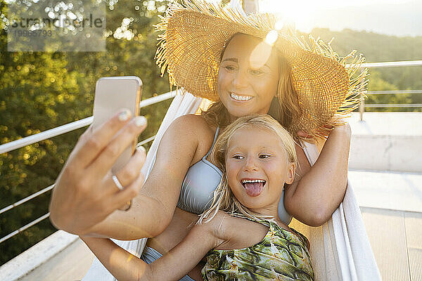 Glückliche Mutter und Tochter machen Selfie mit dem Smartphone in der Hängematte