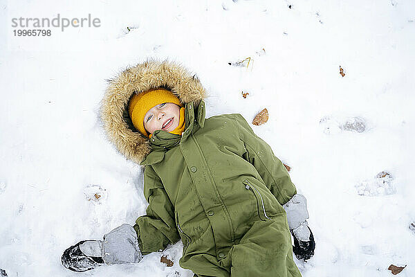Happy boy lying on snow in winter